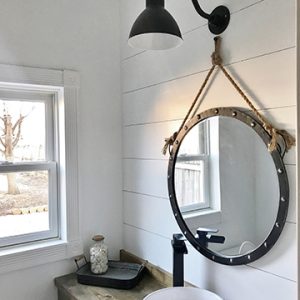 A black gooseneck wall light illuminates a rustic bathroom vanity with a rope-framed mirror