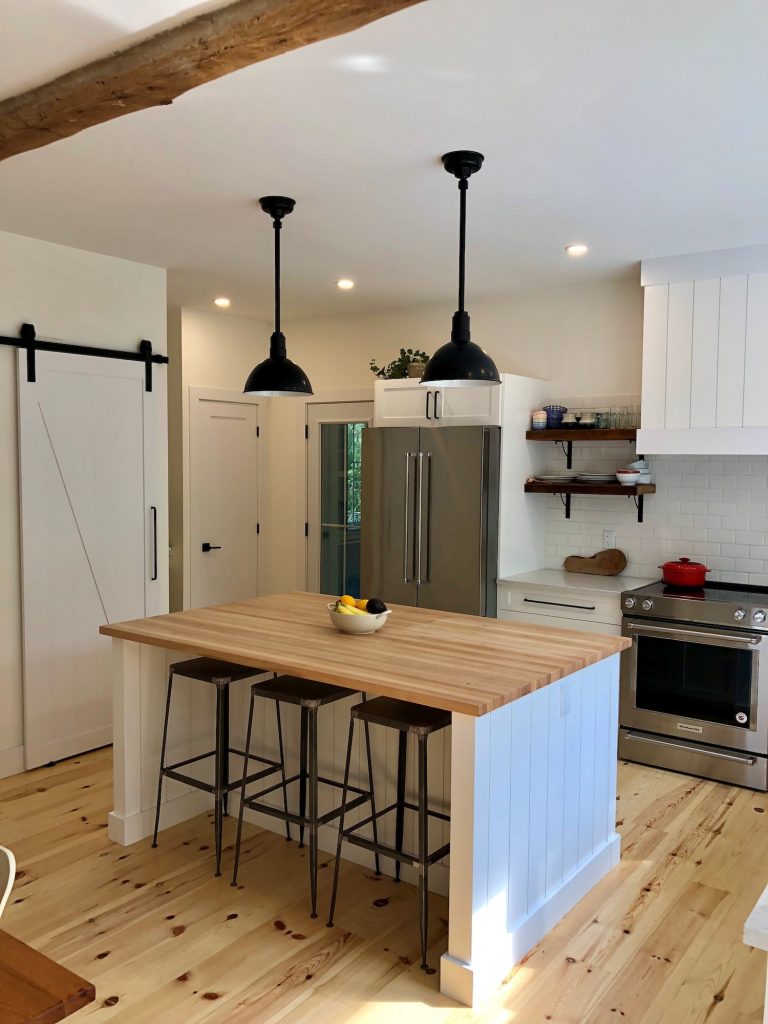 Two black pendant lights hang over a kitchen island with a butcher block countertop