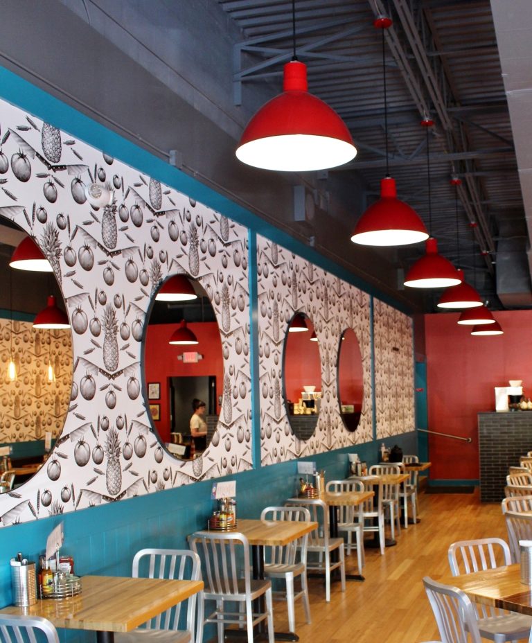 A row of red pendant lights hangs above tables and chairs in a restaurant