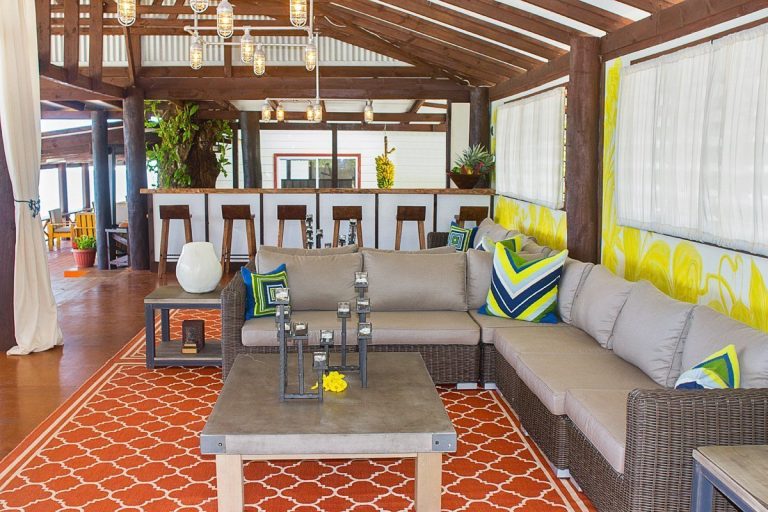A covered outdoor patio area features a sectional sofa, bar stools, and pendant lighting