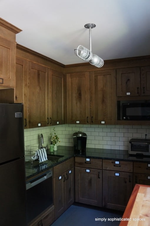 A modern track lighting fixture hangs from the ceiling in a kitchen with dark wood cabinetry