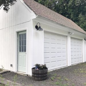 A black gooseneck wall light is mounted on the exterior of a white garage with two garage doors